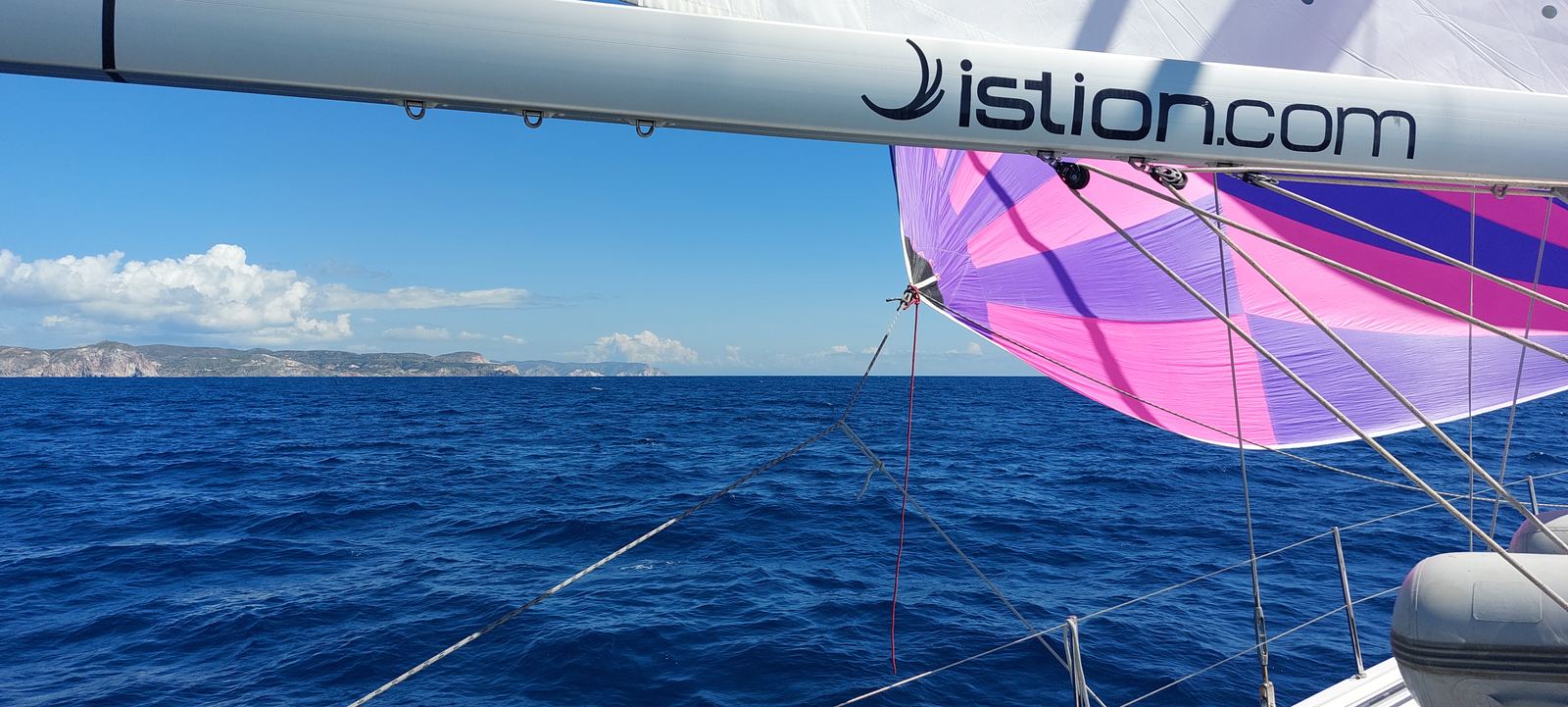 Spinnaker colorato a vento in poppa, costa in lontananza